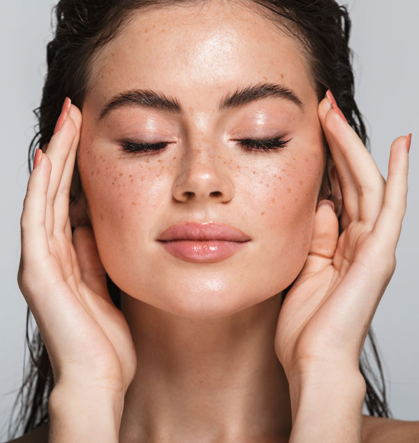 Young woman with freckles touching her temples